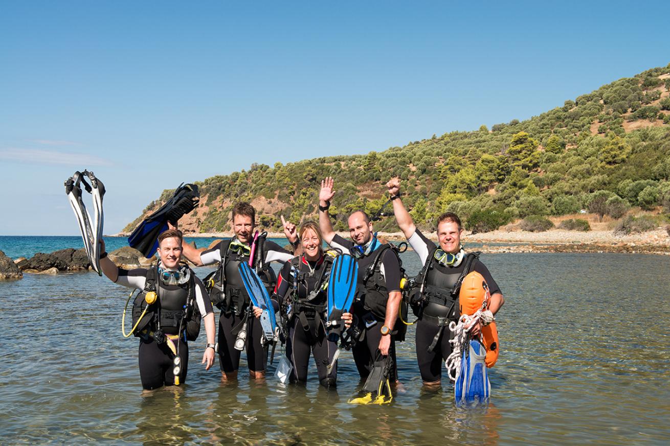 Group of divers stands in water near the shore.