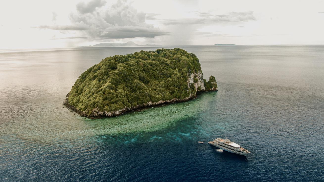 an aerial view of an island and a liveaboard in the foreground