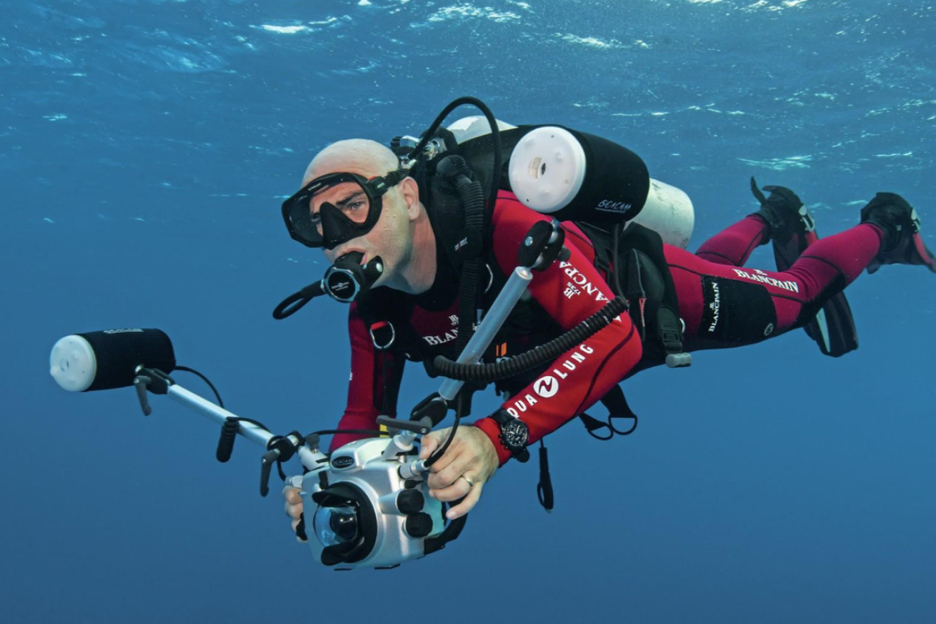 A person in scuba gear underwater holding a camera