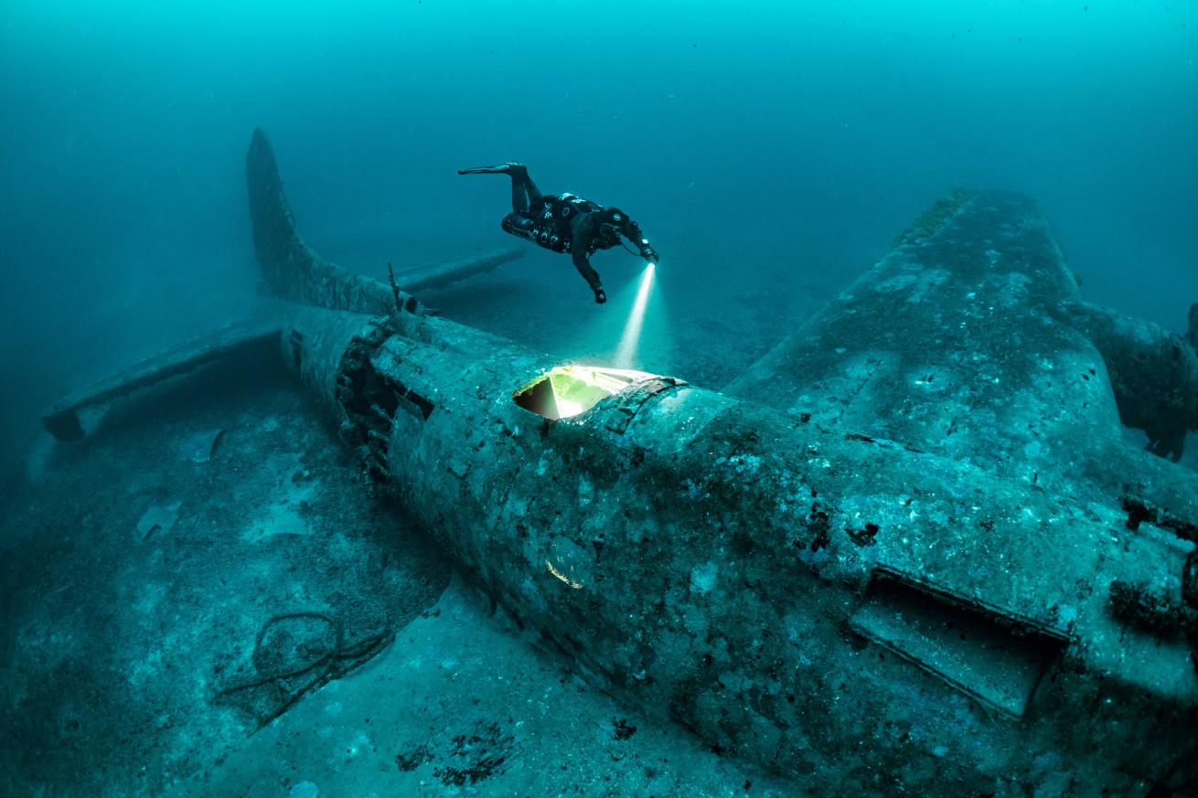 a rebreather diver swimming above a sunken airplane