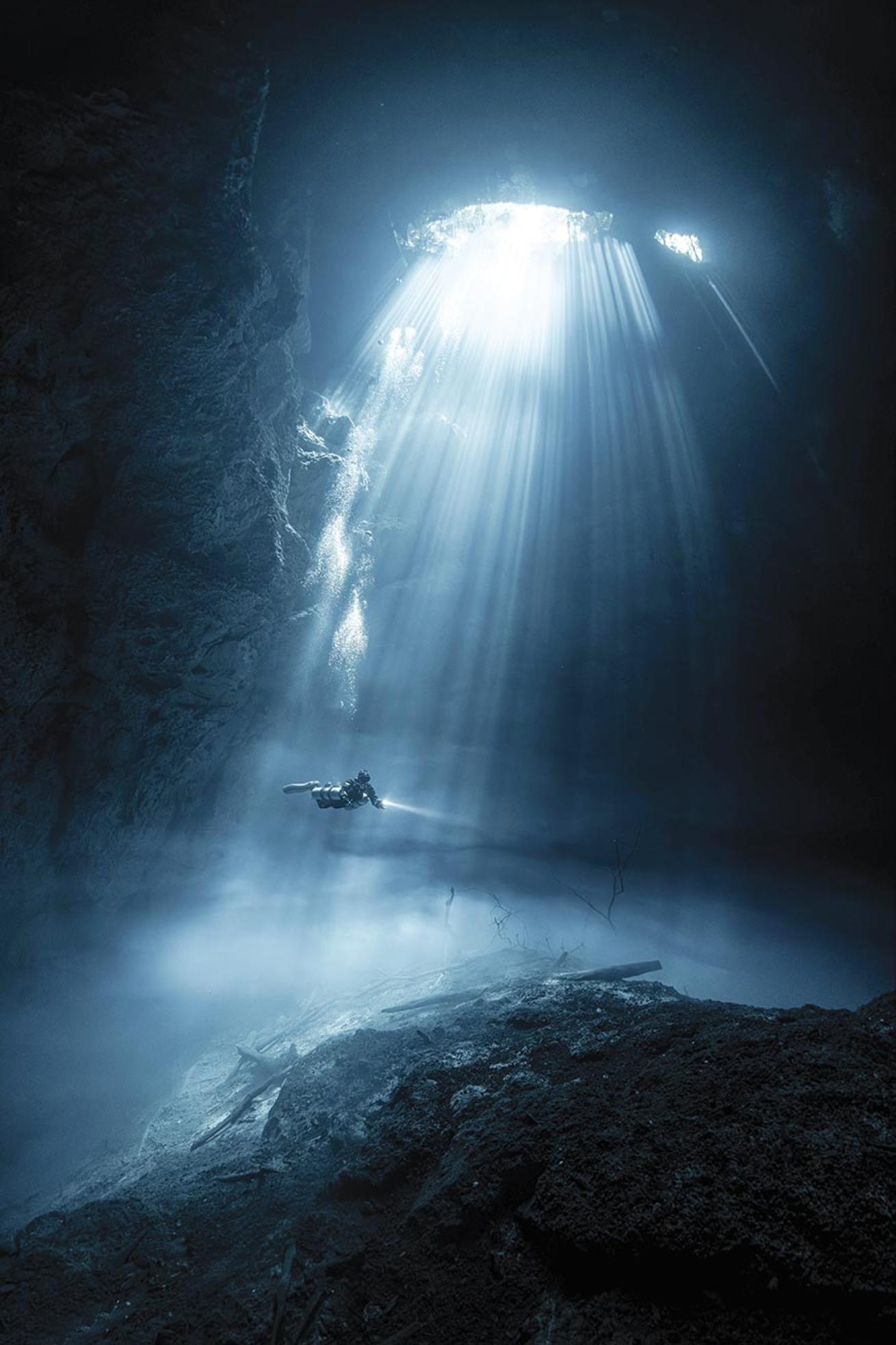 sunbeams in cenote in Mexico El Pit with a diver in the middle surrounded by the cavern