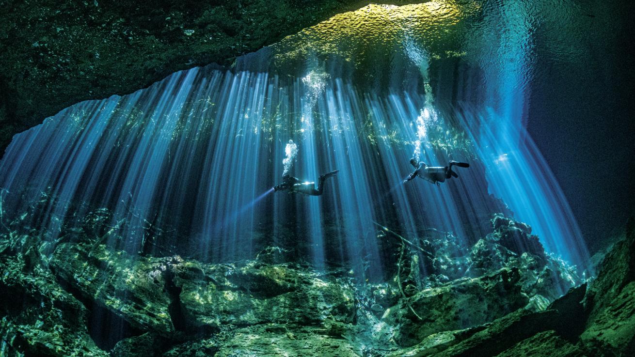 Divers fin through a cenote, careful not to disturb the formations that define the mystique of these otherworldly sites.