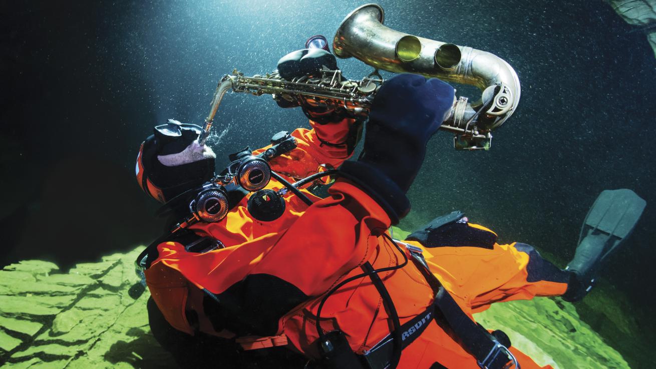 a scuba diver plays a saxophone underwater in Plura cave in Norway