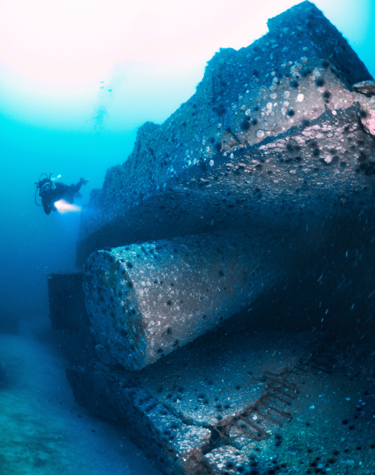 A scuba diver swimming under a large concrete structure.